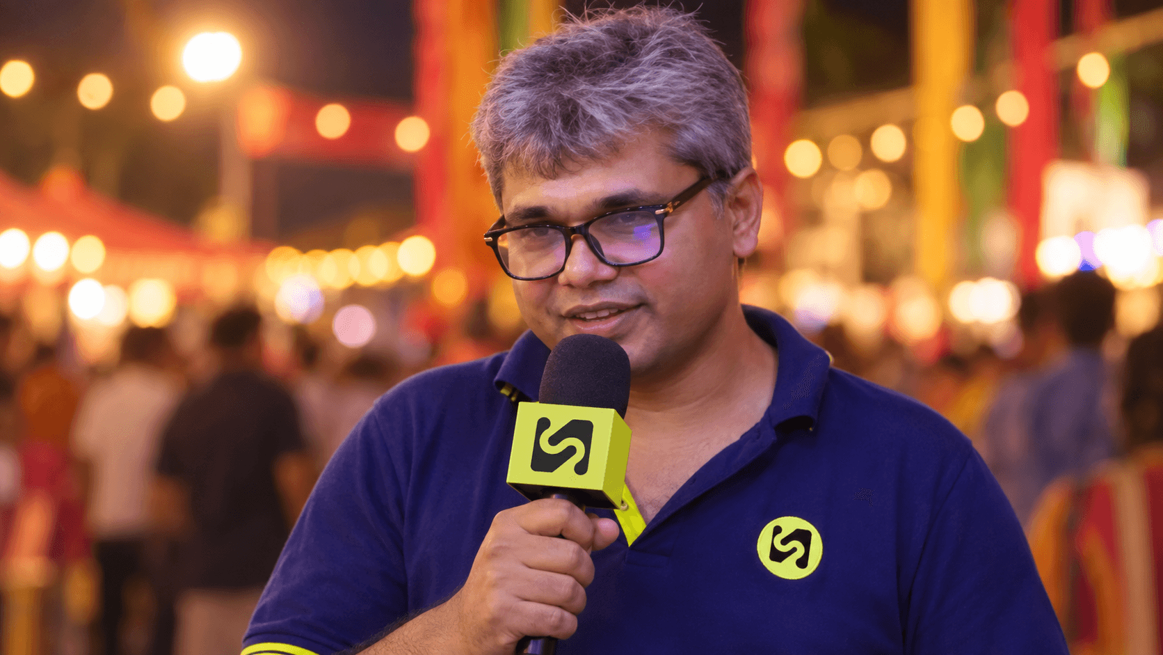 A TV Samadhi presenter speaking into a branded microphone at a festival at night